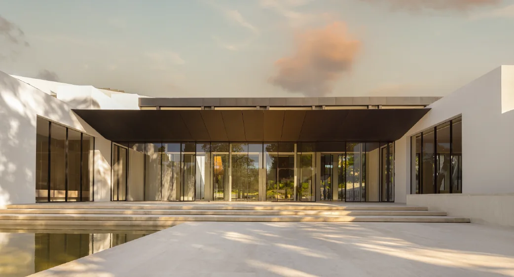 The CAM Centro de Arte Moderna Gulbenkian in Lisbon, with a continuous run of full-height minimal-frame sliding glass doors set beneath a deep bronze canopy above a reflecting pool