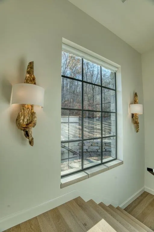 Steel window with narrow black divided-light frames at a stair landing, flanked by driftwood wall sconces