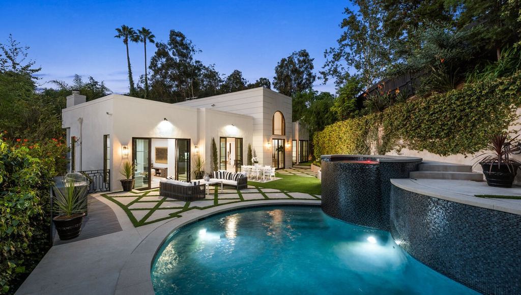 Beverly Hills remodel rear elevation at dusk with black aluminum-clad folding glass doors open to the pool terrace