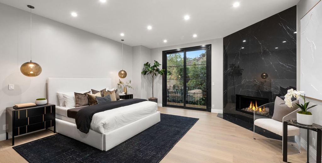 Primary bedroom with a black aluminum-clad French door opening to a balcony beside a black marble fireplace, Beverly Hills remodel