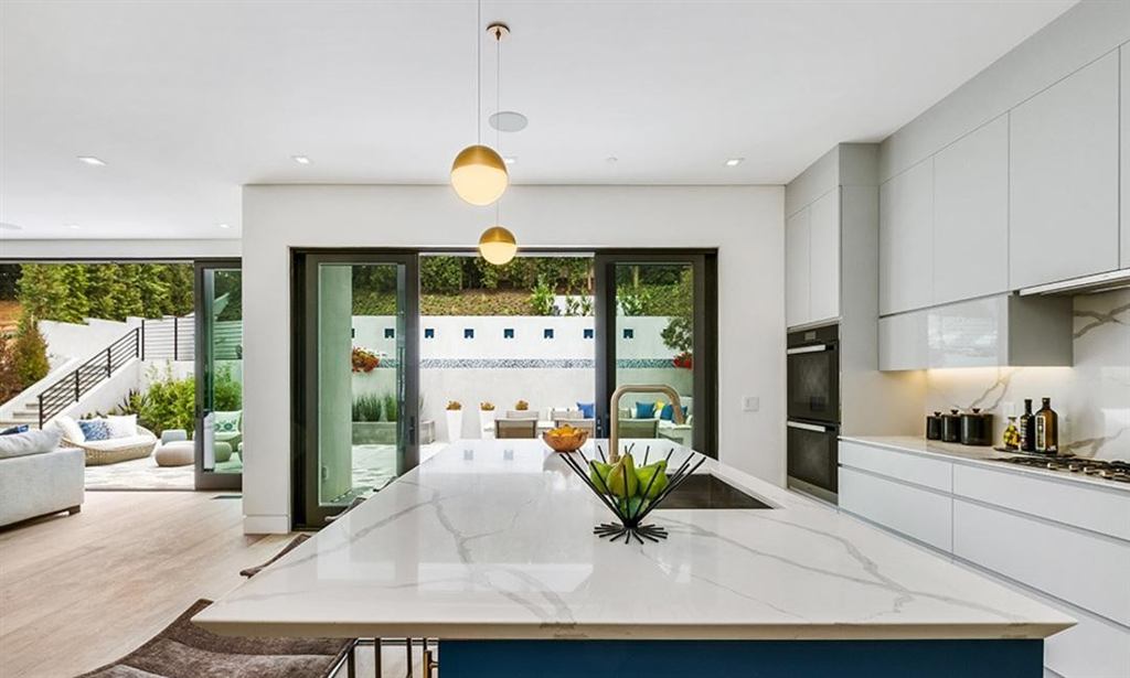 Kitchen with marble island and dark aluminum sliding doors opening to a courtyard, Cheviot Hills