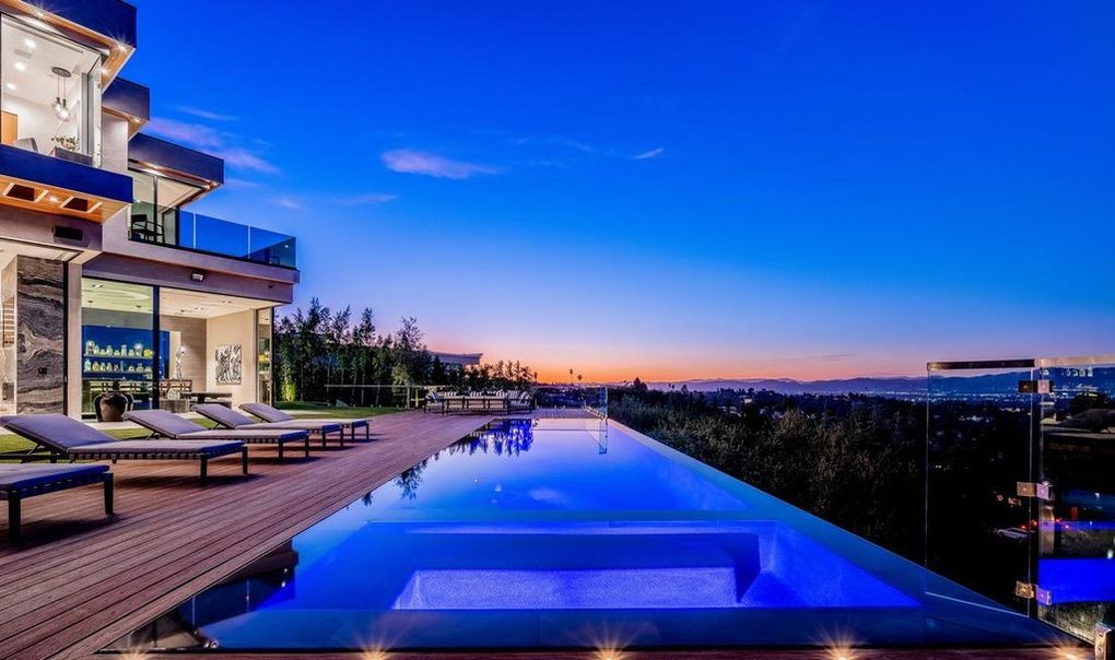 Twilight rear elevation of an Encino new-construction home, infinity pool lit below full-height Arcadia aluminum sliding doors and valley views beyond