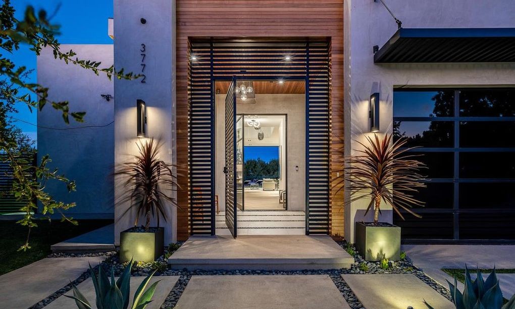 Lit front entry at dusk, Encino new construction, with a glass pivot entry door and Arcadia aluminum windows flanking the approach