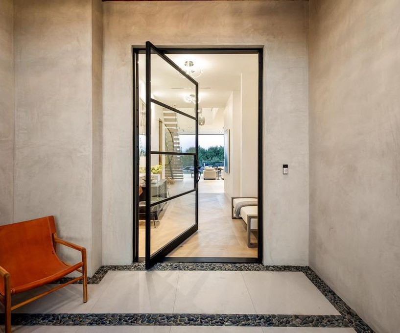 Detail of the Encino entry: a black-framed glass pivot door set into stucco, with the view through the house beyond