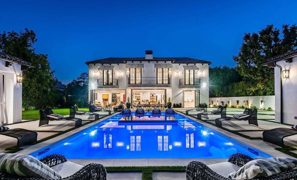 Twilight rear elevation of a Hancock Park new-construction home, with folding wood doors open beneath divided-lite Kolbe wood windows above a lap pool