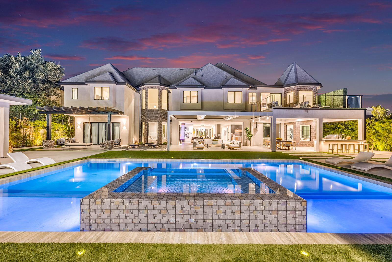 Rear elevation of a Woodland Hills home at dusk with expansive aluminum windows above the pool
