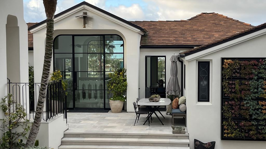 Front patio with a black steel arched entry door wall and dining area, Newport Beach new construction