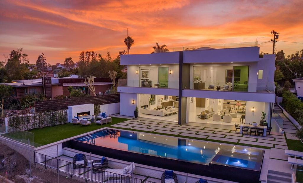 Sunset rear elevation of a Pacific Palisades new-construction home, pool and lit interior behind a fully glazed Arcadia aluminum facade