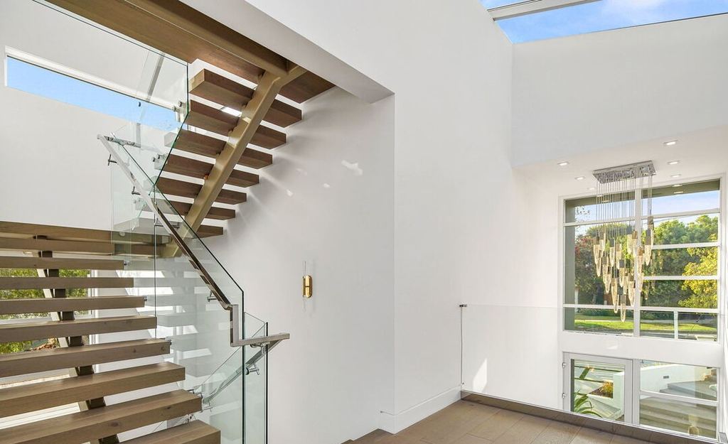 Floating stair with a glass balustrade beside a tall Arcadia aluminum window, Pacific Palisades new construction