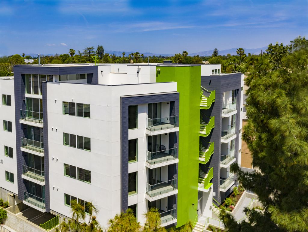 Aerial view of a four-story multifamily building in Studio City with white and green facade panels and glass-railed balconies with aluminum windows