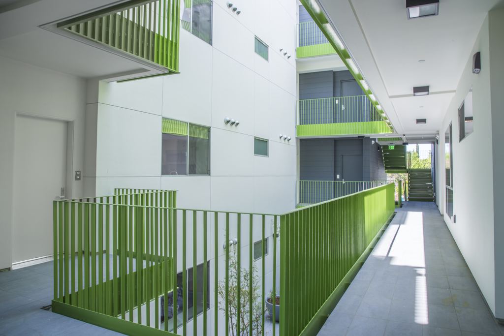 Open-air circulation walkway with green metal railings and aluminum windows along the corridor, Studio City multifamily project