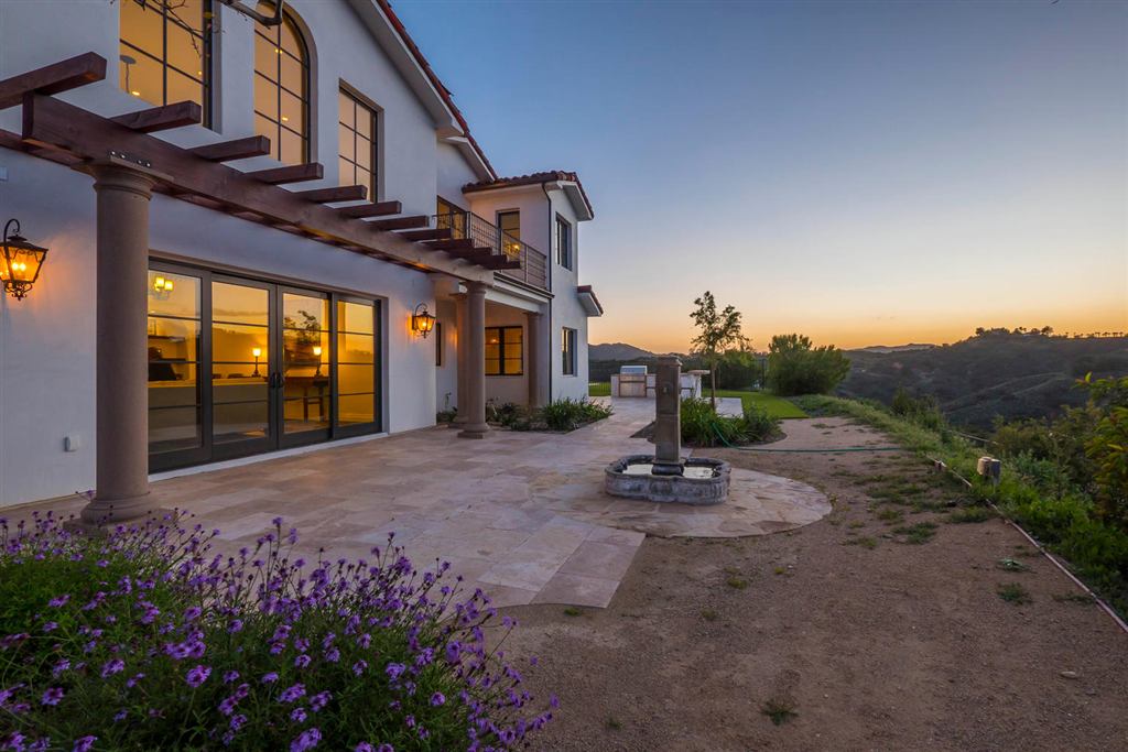 Side patio at sunset with a pergola, stone fountain, and mountain views, Topanga new construction