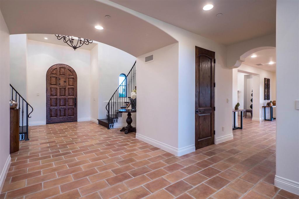 Terracotta-tiled hallway with an arched wood door and curved staircase, Topanga new construction